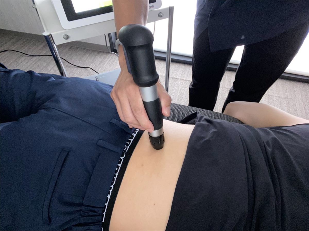 腰まわりへショックマスターの圧力波を照射している施術のようす